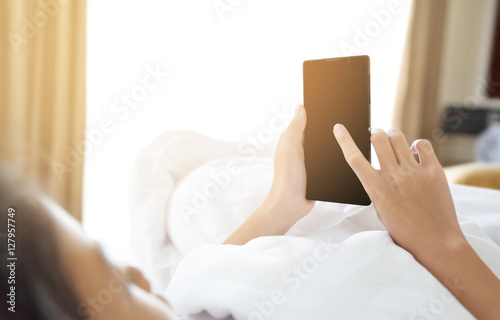 Concentrated young Asian girl looking at her smartphone lying on the bed in bedroom. Technology and internet concept. Copy space. Preteen or school age girl using smart phone on the bed in the morning