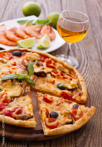 Big tasty pizza with seafood, tomatoes, wine on wooden table