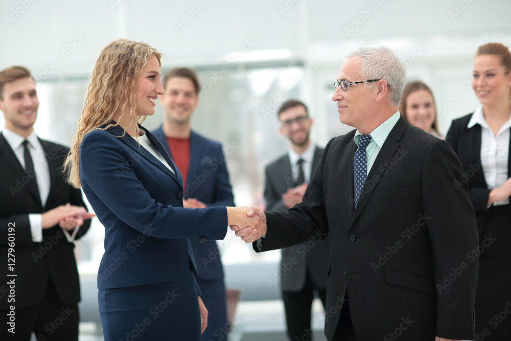 Great job! Two cheerful business people shaking hands while thei Great job! Two cheerful business people shaking hands while thei
