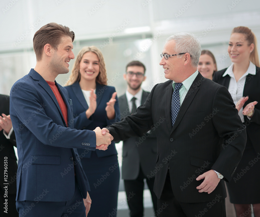 Two cheerful business people shaking hands while their colleague Two cheerful business people shaking hands while their colleague