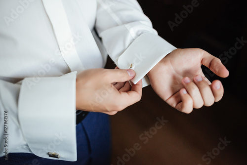 Preparing for wedding. Groom buttoning cufflinks on white shirt before wedding. True men's accessory. Groom's clothes. Close up.