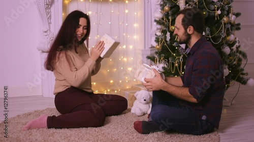 Happy young couple sitting by the fireplace giving each other gifts. Merry Christmas.