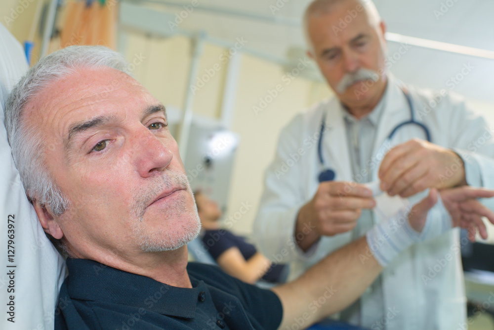 senior doctor putting a bandage on an elder mans arm senior doctor putting a bandage on an elder mans arm