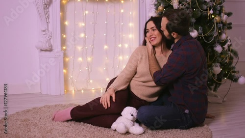 Nice love couple sitting on carpet near the fireplace. Woman and man celebrating Christmas.