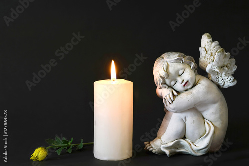 White candle, an angel and flower on dark background