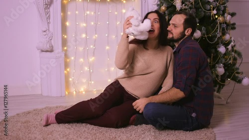 Beautiful young couple laughing and having fun at Christmas. Sitting on the beige carpet in front of the fireplace.