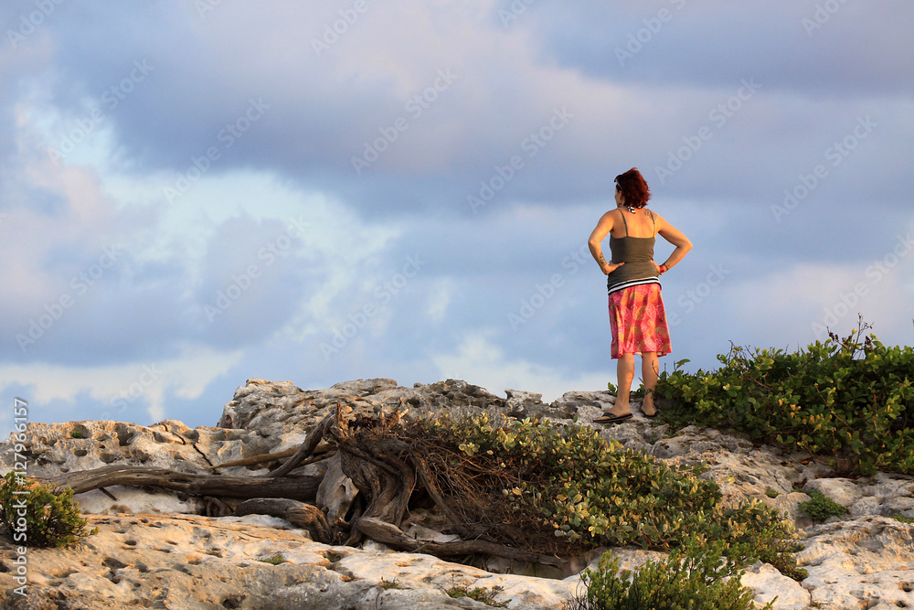 Women in sundress gazing at the view over ocean cliff with hands on hips