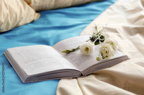 Opened book and beautiful flower on crumpled bed