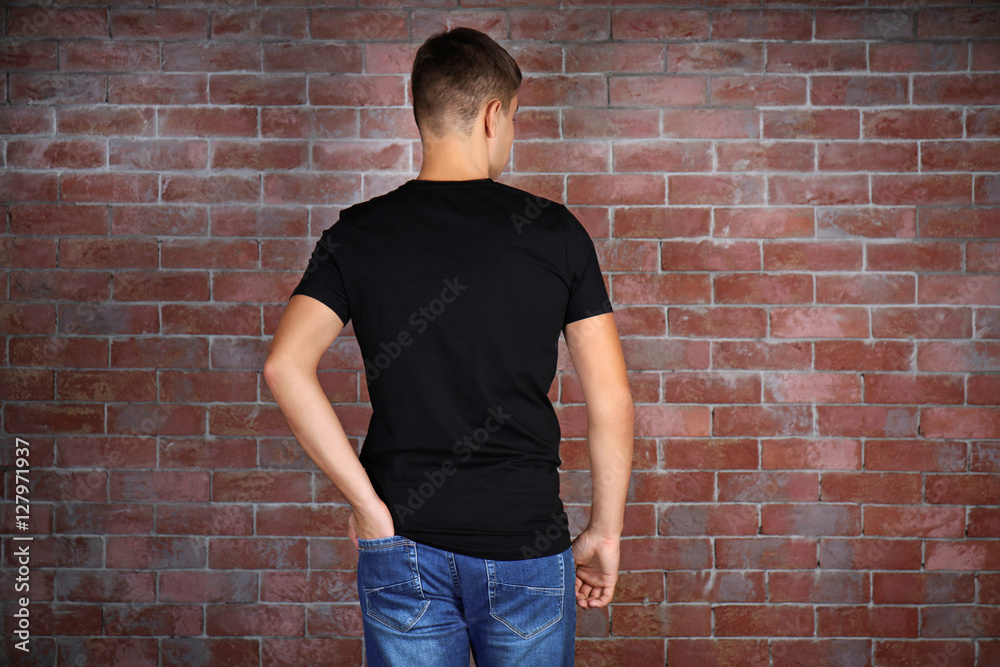 Handsome young man in blank black t-shirt standing against brick wall Handsome young man in blank black t-shirt standing against brick wall