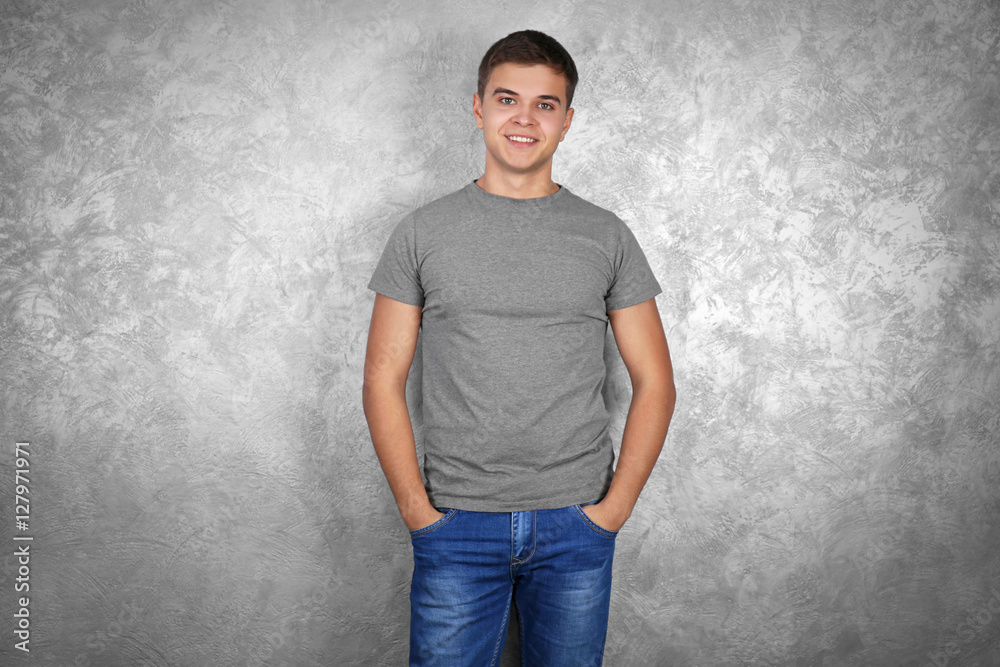 Handsome young man in blank grey t-shirt standing against textured wall Handsome young man in blank grey t-shirt standing against textured wall