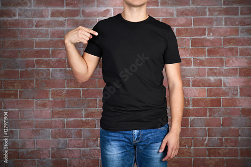 Handsome young man in blank black t-shirt standing against brick wall, close up