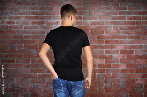 Handsome young man in blank black t-shirt standing against brick wall