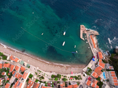 City sandy beach with a pier and coastal dwelling houses in the town of Petrovac. Montenegro, Europe. Aerial view