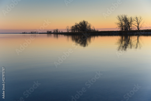 A vibrant  colorful sunset on the lake with trees and land reflected in the background