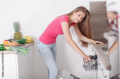 Beautiful young woman made up the dishes in the dishwasher.
