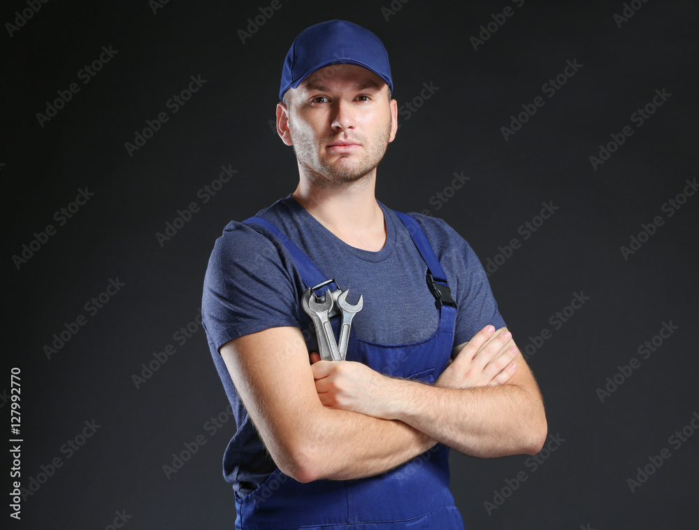 Young mechanic in uniform with crossed arms and wrench standing on a black background Young mechanic in uniform with crossed arms and wrench standing on a black background