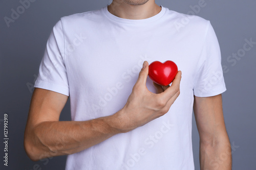 Young man holding red heart on color background