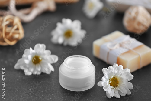 Soap, cream and daisy flowers on grey table