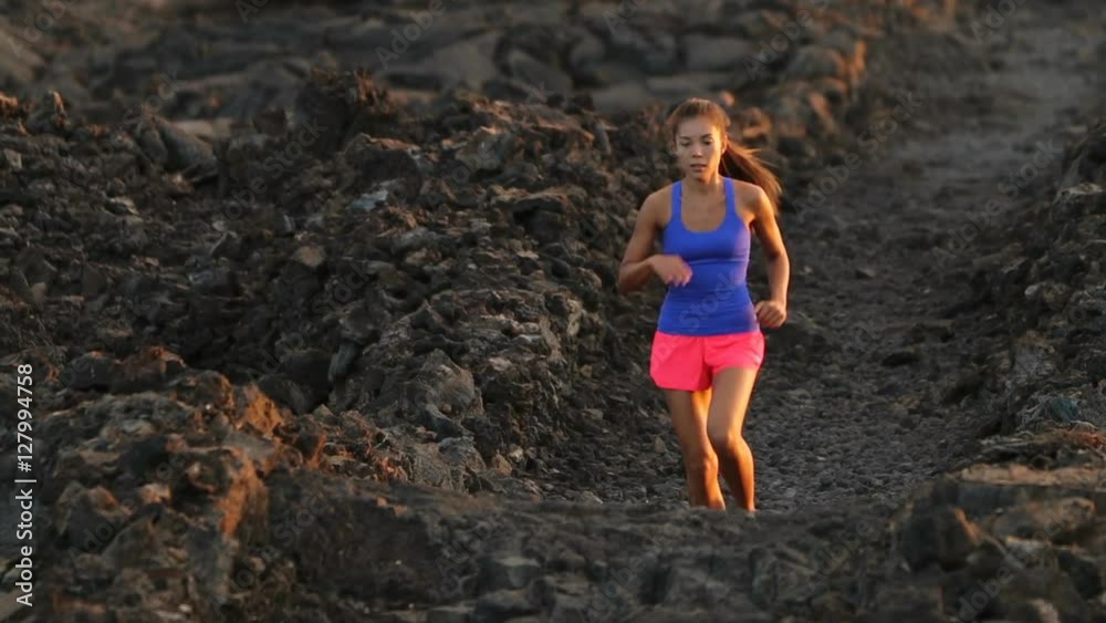 Woman runner running cross country trail run. Female jogger training outside on path outdoors at summer sunset. Beautiful young fitness model with healthy lifestyle . Mixed race Asian Caucasian girl. Woman runner running cross country trail run. Female jogger training outside on path outdoors at summer sunset. Beautiful young fitness model with healthy lifestyle . Mixed race Asian Caucasian girl.