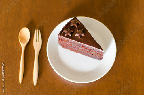 Piece of dark chocolate cake on white dish with wooden spoon ready to eating