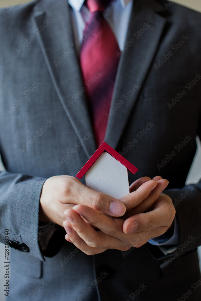 Business man in suit having miniature house on palm of his hand - Business mortgage, property loan, house insurance, business investment concept