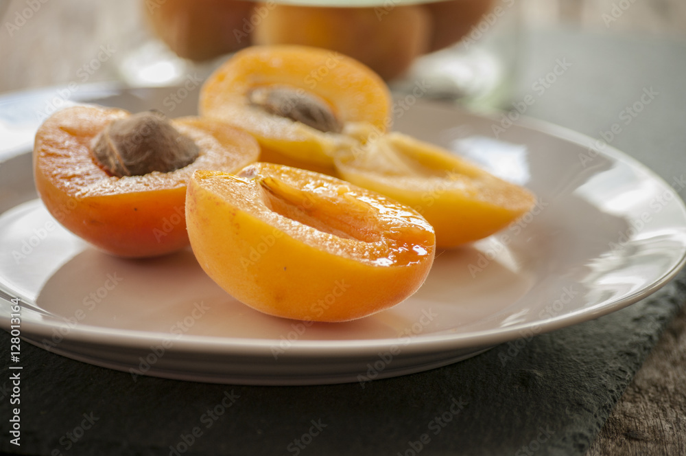 Whole orange apricots with red blush, from above, space for text. Open apricot with stone and leaves. On rustic white wood.