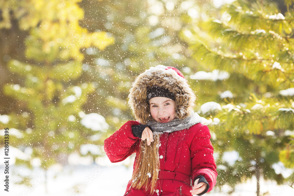 Portrait of little girl in red jacket plays with a snow in park in winter