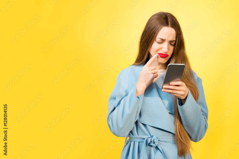 Portrait of confused woman with mobile phone on the yellow background Portrait of confused woman with mobile phone on the yellow background