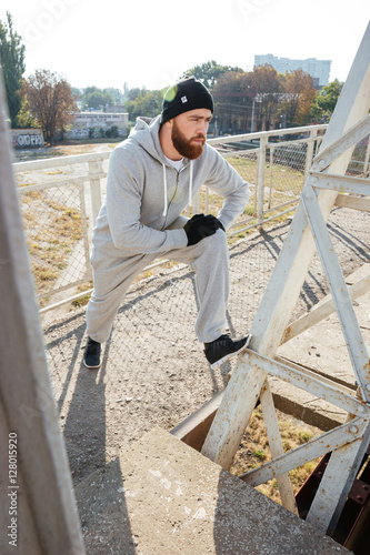 Confident bearded male athlete stretching and warming up before jogging