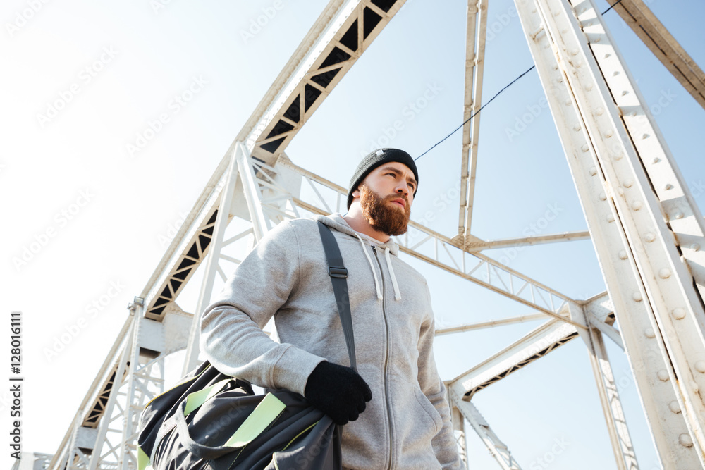 Portrait of an athlete with sports bag walking along bridge