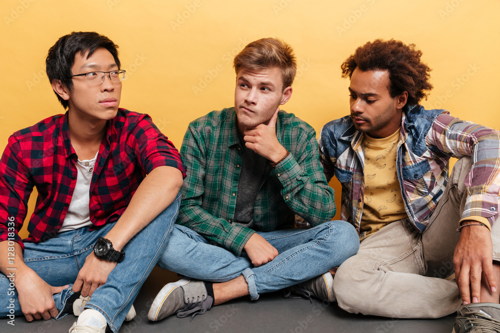 Multiethnic group of three thoughtful men friends sitting and thinking Multiethnic group of three thoughtful men friends sitting and thinking