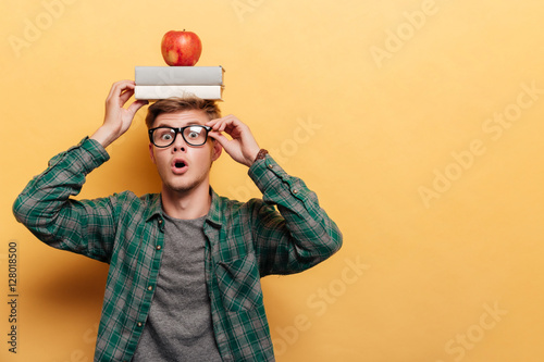 Astonished man student with book and apple on his head