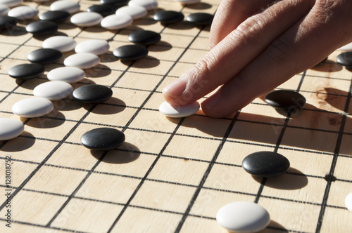 Close up view of hand playing black and white stone pieces on Chinese go game board. Outside activity with natural sun light.