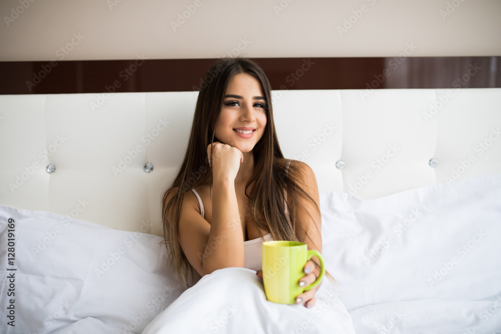 attractive young woman drinking coffee while sitting in bed