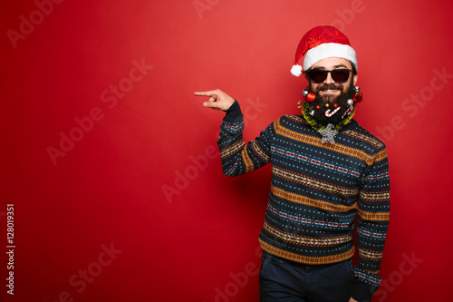 Bearded hipster man in santa hat gesturing to left
