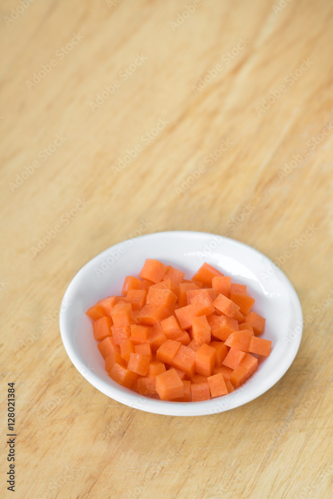 Carrot cubes in white cup on wooden cutting board Carrot cubes in white cup on wooden cutting board