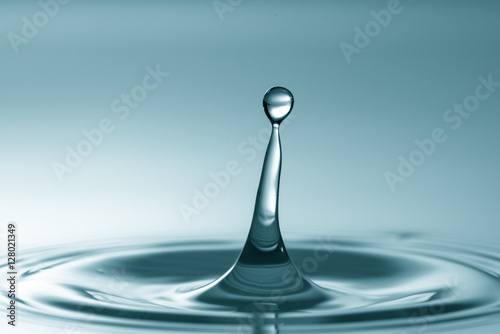 Water drop falling and drips on water mirror. Drops splash and make perfect circles on water surface