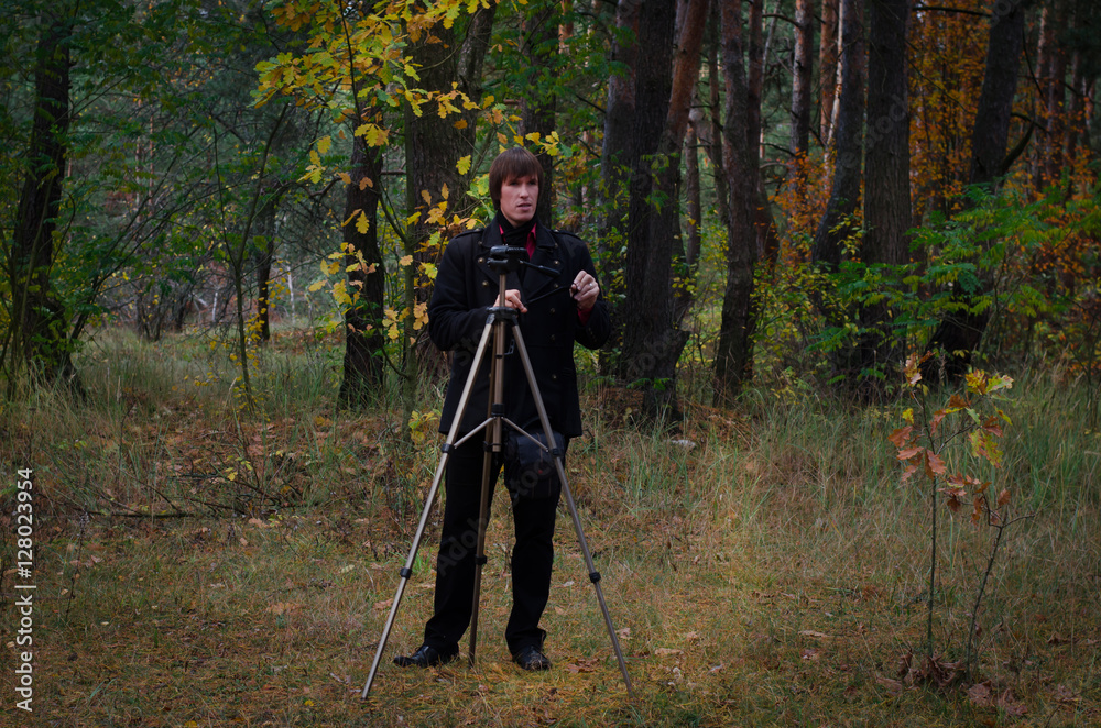 a guy with a tripod in the forest   