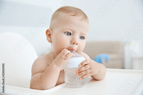 Little baby drinking water from bottle indoors