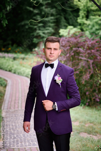 handsome and young groom in blue suit standing outdoors