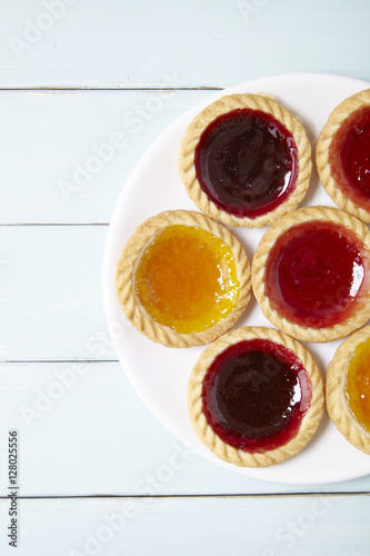 Fototapeta Naklejka Na Ścianę i Meble -  Aerial view of a plate full of assorted fruit jam tarts on a blue wooden table top background