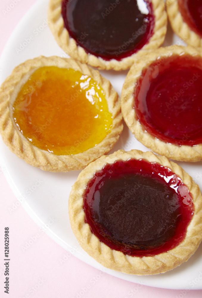 A plate full of assorted fruit jam tarts on a pastel pink background A plate full of assorted fruit jam tarts on a pastel pink background
