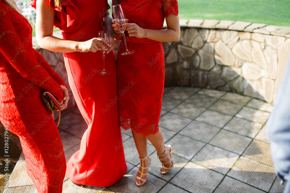Women in red stand with champagne flutes in their hands