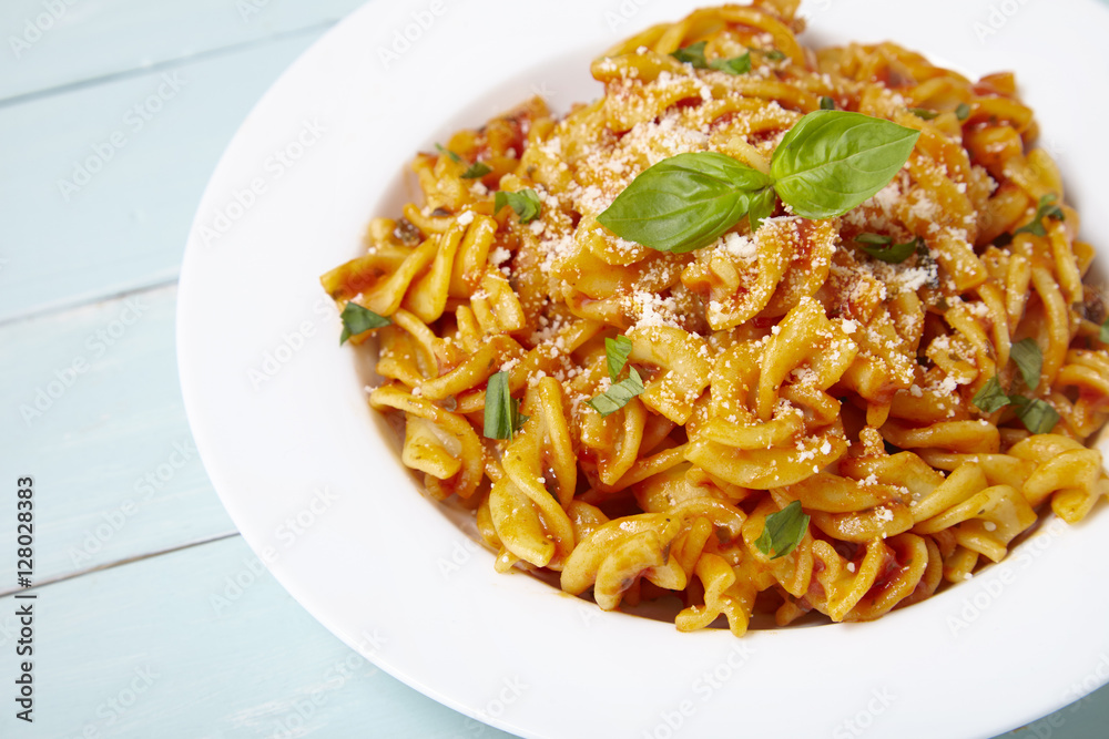 A dinner dish full of tomato and basil fusilli pasta on a blue wooden dining table background with empty space at side