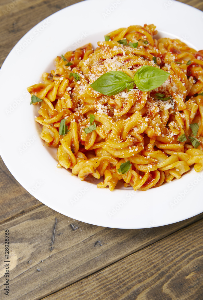 A dinner dish full of tomato and basil fusilli pasta on a rustic wooden dining table background A dinner dish full of tomato and basil fusilli pasta on a rustic wooden dining table background