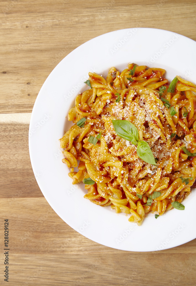 Overhead view of a dinner dish full of tomato and basil fusilli pasta on a wooden kitchen counter background