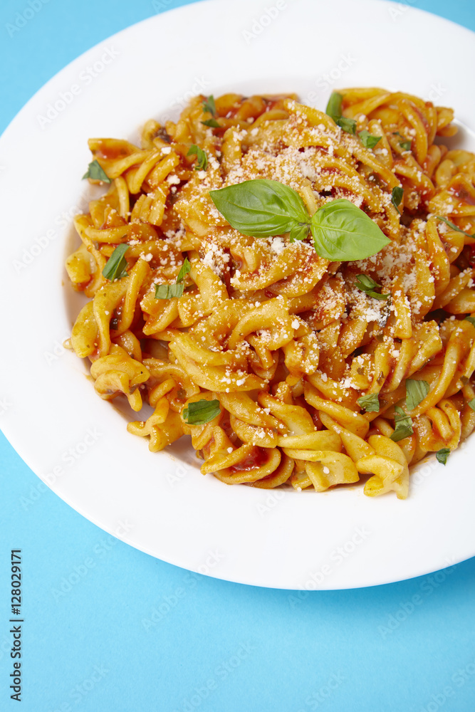 A dinner dish full of tomato and basil fusilli pasta on a bright blue background