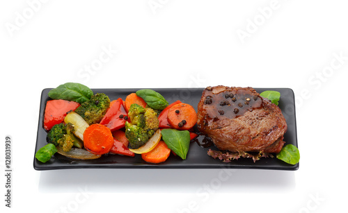 Veal steake with vegetables on a black plate isolated on white background photo