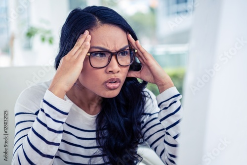 Fotografie Frowning Asian woman looking at laptop with hands on head
