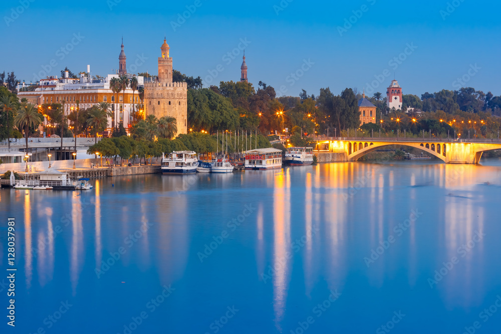 Dodecagonal military watchtower Golden Tower or Torre del Oro and bridge Puente San Telmo during evening blue hour, Seville, Andalusia, Spain